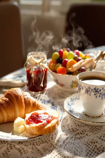 Table de petit-déjeuner en France : croissant, baguette, café et fruits frais au soleil levant