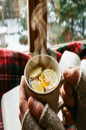 Mains tenant une tasse fumante d’infusion gingembre citron miel, ambiance hivernale réconfortante