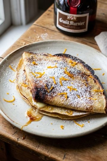 Assiette de crêpes maison au Grand Marnier pliées en triangle, saupoudrées généreusement de sucre glace et zestes d'orange