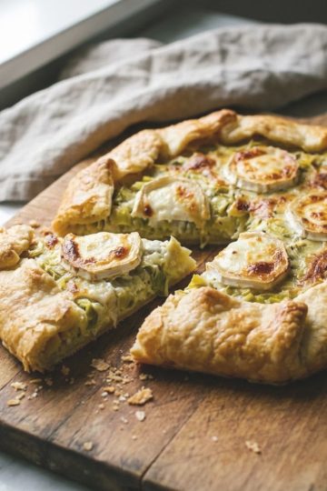 Tarte rustique poireaux chèvre dorée et croustillante présentée sur une planche en bois avec une part découpée