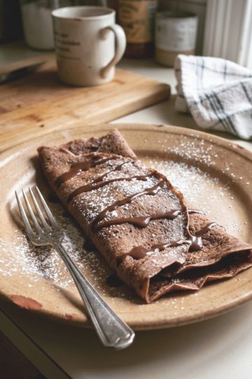 Une crêpe au chocolat maison pliée de manière décontractée sur une assiette rustique avec une fourchette