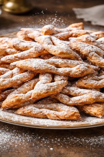 Montagne de bugnes lyonnaises croustillantes saupoudrées de sucre glace sur un plat en céramique