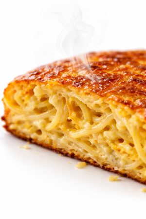 Gros plan sur la texture intérieure d'une part de frittata spaghettis montrant les couches d'œuf coagulé et de pâtes dorées
