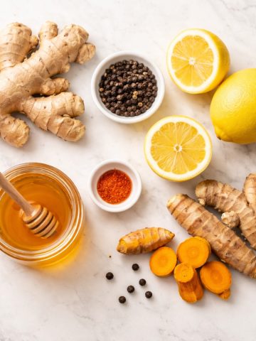 Ingrédients recette shot immunité gingembre citron curcuma poivre miel à plat sur marbre blanc