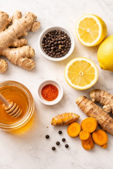 Ingrédients recette shot immunité gingembre citron curcuma poivre miel à plat sur marbre blanc