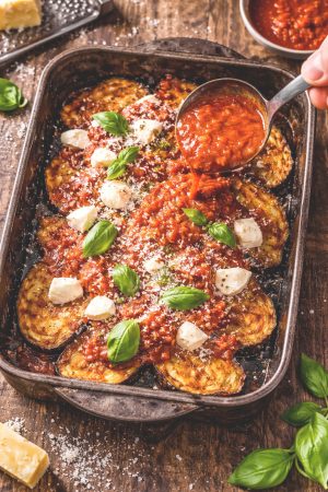 Montage de la parmigiana d'aubergines couche par couche dans un plat rectangulaire avec sauce tomate, mozzarella et parmesan
