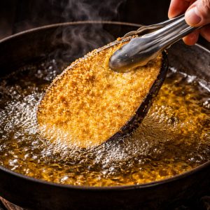 Tranche d'aubergine panée plongeant dans l'huile chaude à 170°C avec des bulles vives autour pour une friture croustillantepng