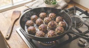 Boulettes d'agneau en train de dorer dans une poêle en fonte, disposées sans se toucher, avec une belle croûte dorée