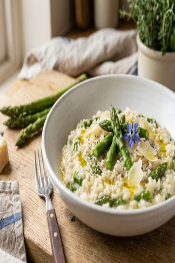 Risotto crémeux aux asperges vertes en assiette creuse blanche, copeaux de parmesan et fleur de bourrache
