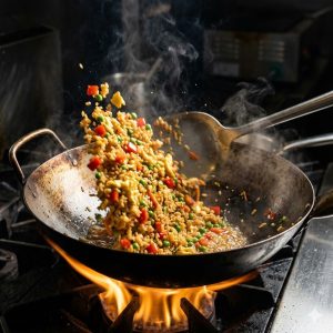 Riz sauté aux légumes et œuf en train de cuire dans un wok fumant à feu vif, technique wok express