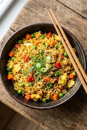 Riz sauté aux légumes et œuf servi dans un bol asiatique, garni d'oignons nouveaux et graines de sésame