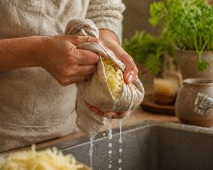 mains de cuisinière) tordant un torchon en lin beige au-dessus d'un évier, l'eau s'écoulant entre les doigts