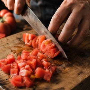 Découpe de tomates fraîches en brunoise au couteau sur une planche en bois