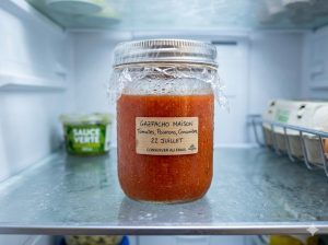 Gaspacho maison versé dans un bocal en verre hermétique filmé, prêt à être conservé au réfrigérateur