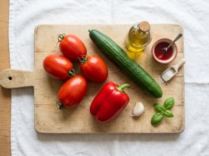 Ingrédients du gaspacho andalou disposés sur une planche en bois : tomates mûres, concombre, poivron rouge, ail, huile d'olive et vinaigre