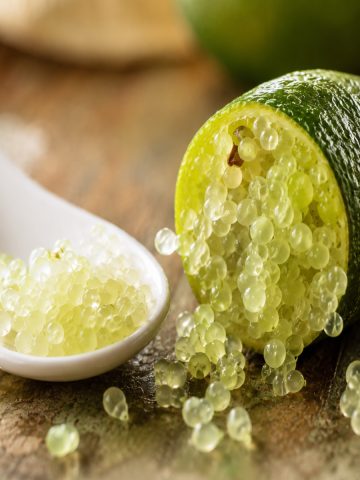Perles de citron caviar tranché disposées sur une cuillère blanche, prêtes à garnir un plat.