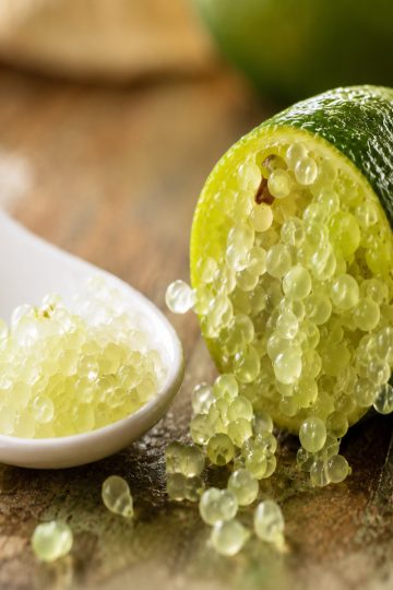 Perles de citron caviar tranché disposées sur une cuillère blanche, prêtes à garnir un plat.