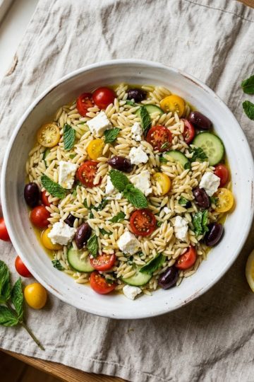 Salade de pâtes orzo feta tomates cerises dans un grand bol blanc, vinaigrette citronnée, menthe fraîche, vue du dessus