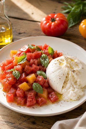 Tartare de tomates fraîches et burrata crémeuse, huile d'olive et basilic, servi sur une assiette en céramique blanche
