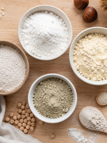 Bols de farines sans gluten variées : riz, châtaigne, pois chiche, sarrasin, sur plan de travail clair