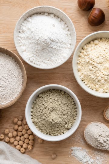 Bols de farines sans gluten variées : riz, châtaigne, pois chiche, sarrasin, sur plan de travail clair