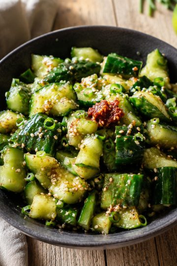 une salade de concombre créole servie en dôme dans un bol sombre, avec sésame et piment