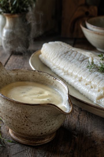 Beurre blanc nantais ivoire et mousseux dans une saucière rustique, servi avec un filet de poisson poché