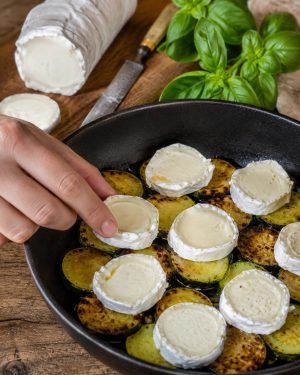 Bûche de chèvre coupée en rondelles ajoutée sur les courgettes chaudes