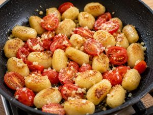 Tomates cerises et ail ajoutés aux gnocchis dans la poêle
