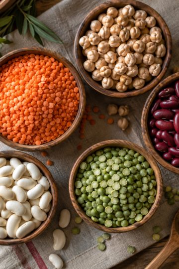Assortiment de légumes secs dans des bols en bois : lentilles, pois chiches, haricots rouges et blancs