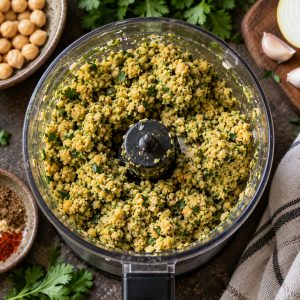 Pâte à falafels granuleuse dans le bol du robot avec herbes et épices
