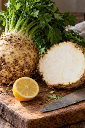 Céleri-rave entier et coupé en deux sur une planche en bois avec un citron
