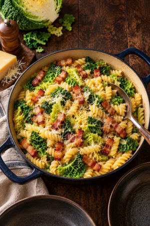 Sauteuse de pâtes au chou vert et lardons fumés sur une table en bois